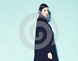 Fashion concept. Girl on strict confident face in long black coat, grey background. Lady with red lips looking at camera