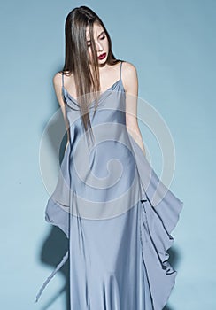 Fashion concept. Girl on strict confident face in long blue dress, light blue background. Lady with red lips wears