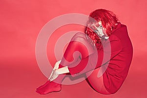 Fashion concept. Lady looking at camera and sits on floor. Woman with makeup and red wig posing in total red outfit