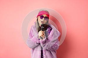 Fashion concept. Stylish senior asian woman singing karaoke, perform on stage with microphone, wearing trendy sunglasses