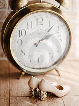 Fashion concept. Wedding bridal shoes and vintage alarm clock. High hell beige female shoes, fashion concept. Symbol of fashion`
