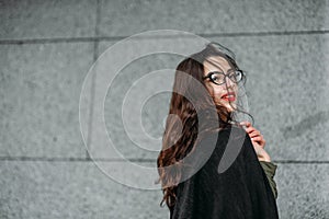 Fashion consept: beatiful young girl with long hair, glasses, red lips standing near modern wall wearing in green suit and grey je