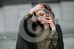 Fashion consept: beatiful young girl with long hair, glasses, red lips standing near modern wall wearing in green suit and grey je