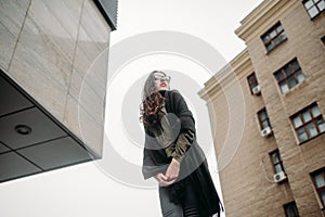 Fashion consept: beatiful young girl with long hair, glasses, red lips standing near modern wall wearing in green suit and grey je