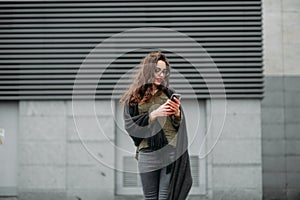 Fashion consept: beatiful young girl with long hair, glasses, red lips standing near modern wall wearing in green suit and grey je