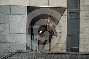 Fashion consept: beatiful young girl with long hair, glasses, red lips standing near modern wall wearing in green suit and grey je