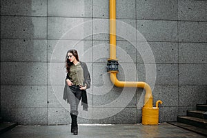 Fashion consept: beatiful young girl with long hair, glasses, red lips standing near modern wall wearing in green suit and grey je