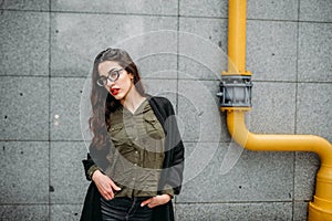 Fashion consept: beatiful young girl with long hair, glasses, red lips standing near modern wall wearing in green suit and grey je