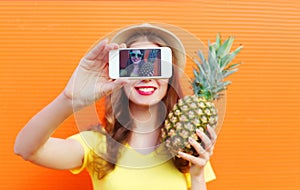 Fashion cool girl with pineapple taking picture self portrait on smartphone over colorful
