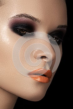 Fashion dark smoky eyes makeup, black eyeshadows, orange lips.