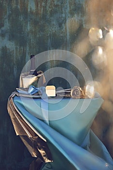 Fashion decoration with blue, turquoise and gold cloth, bottle of champagne with bow on the blue rusty background