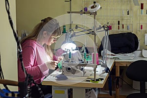 Fashion designer clothes sews on sewing machine by light lamp in workshop