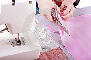 Fashion designer concept. Womans hands cutting pink fabric in studio