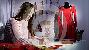 Fashion designer draws a sketch of a red dress, outside the window already evening