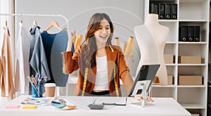 Fashion designer l young asian woman working using laptop, tablet and smiling while standing in workshop Responding on business e-