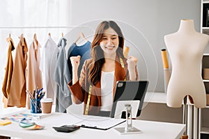 Fashion designer l young asian woman working using laptop, tablet and smiling while standing in workshop Responding on business e-