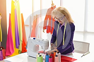 Fashion designer studio measuring textile material scissors cutting fabric by senior woman designer stylish showroom hanging