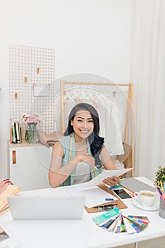 Fashion designer at work. Happy young Asian woman drawing while sitting at her working place in fashion workshop