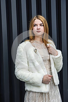 Fashion. Elegant woman in beige dress wearing in white fur coat. Beautiful girl model in luxurious clothes posing on abstract