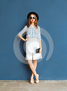 Fashion elegant woman in a black hat, white skirt with a handbag clutch