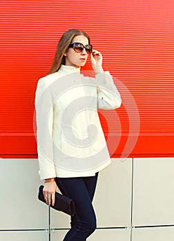 Fashion elegant woman wearing a white coat jacket with clutch bag over red