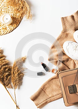 Fashion flat lay with beige, caramel sweater casual fall or winter look with sneakers, lipstick and pampas grass on white