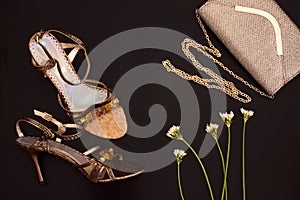 Fashion flat lay. Formal evening wear: golden chain bag and high heels on dark background with flowers