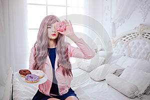 Fashion freak. Glamour synthetic girl, fake doll with empty look and long lilac hair is holding pink donut in front of
