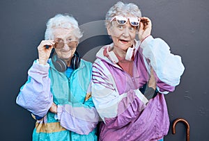 Fashion, funky and friends with a senior woman pair standing outdoor on a gray wall background together. Silly, style