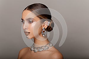 Fashion girl beauty portrait. Young woman with jewelry, hair arranged, makeup, looks to the side, with bare shoulders.