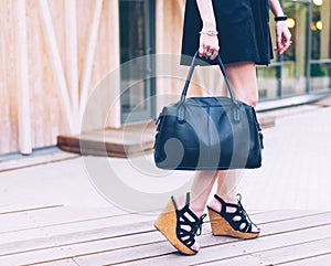 Fashion. A girl in a black dress and with a fashionable handbag is standing on the veranda of a summer cafe