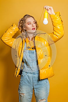 Fashion girl holding light bulb on yellow background