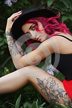 Fashion girl with red hair and big round hat, spring portrait in lilac colors in summer. Beautiful red pink dress, tattoos on the photo