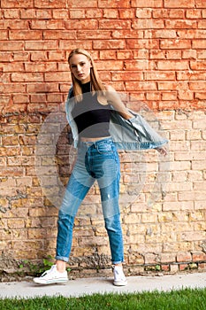 fashion girl standing near brick wall in denim and sneakers. Vogue Style