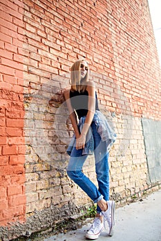 fashion girl standing near brick wall in denim and sneakers. Vogue Style