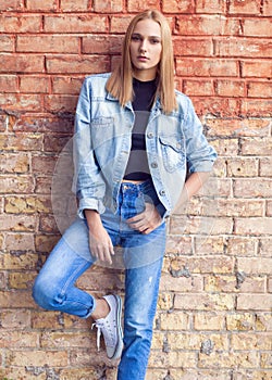 fashion girl standing near brick wall in denim and sneakers. Vogue Style