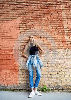 fashion girl standing near brick wall in denim and sneakers. Vogue Style