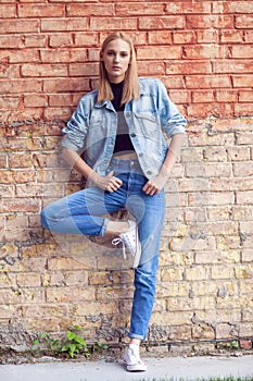 fashion girl standing near brick wall in denim and sneakers. Vogue Style