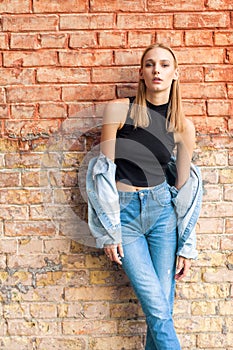 fashion girl standing near brick wall in denim and sneakers. Vogue Style