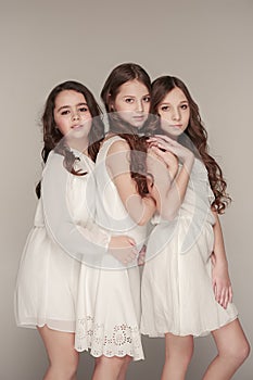 The fashion girls standing together and looking at camera over gray studio background