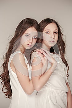 The fashion girls standing together and looking at camera over gray studio background