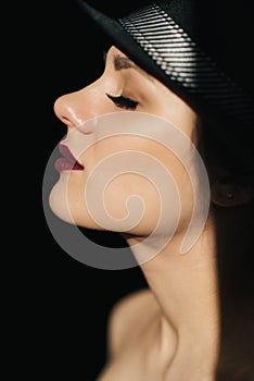 Fashion portrait in profile of a young sexy girl in a black hat with red lipstick