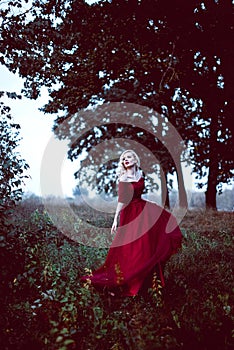 Fashion gorgeous young blonde woman in beautiful red dress in a fairy-tale forest. magic atmosphere. Retouched toning shot