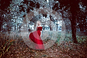 Fashion gorgeous young blonde woman in beautiful red dress in a fairy-tale forest. magic atmosphere. Retouched toning shot