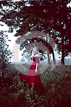 Fashion gorgeous young blonde woman in beautiful red dress in a fairy-tale forest. magic atmosphere. Retouched toning shot