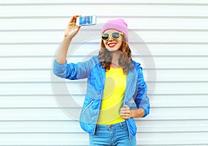 Fashion happy cool smiling girl in colorful clothes taking picture makes self portrait on smartphone over white background