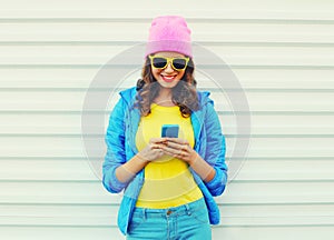 Fashion happy cool smiling girl using smartphone in colorful clothes over white background wearing pink hat yellow sunglasses