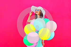 Fashion happy pretty smiling woman with an air colorful balloons is having fun in summer over a pink background