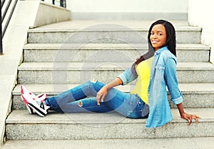 Fashion happy smiling young african woman wearing jeans clothes sitting resting on stairs
