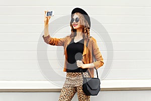 Fashion happy young smiling woman taking photo picture self-portrait on smartphone wearing retro elegant hat, sunglasses